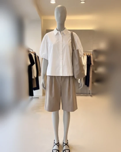 A store mannequin in a white blouse and taupe shorts